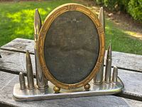 Front view of the trench art solid brass oval picture frame with bullet-shaped accent decorations on a rectangular base, showing detailed border and bullet motifs.