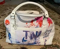 Front view of white Aritzia TNA tote bag with colorful print and metal clover charm on front