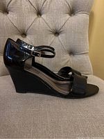Side view of black patent leather wedge sandal showing ankle strap and wedge heel.