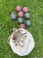 Set of bocce balls arranged on grass next to the white canvas carrying bag showing wear and drawstring closure.