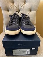 Front view of the navy blue leather sneakers placed on top of original Cole Haan box showing condition and design details.