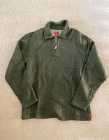 Full view of the green Guess quarter zip pullover laid flat on carpet.