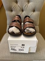 Front view of Josef Seibel men's leather sandals on original box, showing adjustable straps and toe area with paper stuffed inside.