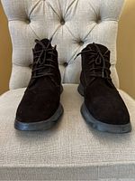Front view of the pair of men's brown suede lace up boots placed on a beige tufted chair.