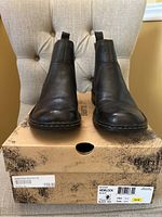 Front view of black leather Chelsea boots on original Born box, showing light creasing and wear on toe and upper.