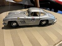 Side profile of silver Mercedes Benz 300SL die cast model car with racing decals and checkered stripe on hood and roof.