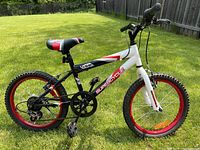 Side view of the kids 18 inch mountain bike showing white and black frame, red rims, knobby tires, adjustable seat and kickstand.