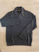 Full top view of dark grey textured knit shawl collar sweater laid flat on carpet.