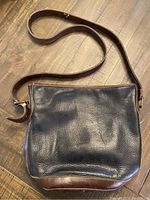 Front view of Roots black leather crossbody bag showing black pebble grain leather and brown leather trim.