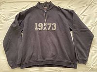 Full front view of navy blue Roots sweatshirt laid flat showing overall design, oversized fit, and faded graphic 1973 on chest.