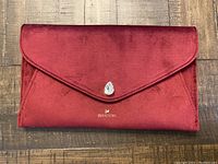 Front view of red velvet Swarovski clutch lying flat showing flap with teardrop crystal detail and logo below.