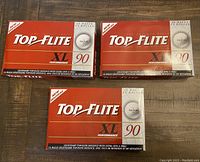 Three unopened boxes of Top Flite XL Performance golf balls placed on a wooden surface. Each box labeled containing 15 balls except one with 13 balls.