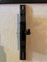 Close-up shot of the TV wall mount showing adjustable slot and knob on a beige carpet.