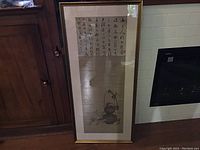 Overall view of framed artwork leaning against cabinet and fireplace