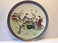 Front view of Asian porcelain plate showing painted traditional figures and blue and gold rim.