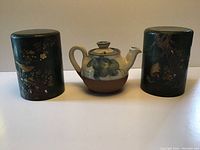 Full set including the ceramic teapot centered between two black decorative canisters with Asian style designs.