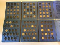 Top view of six vintage blue coin folders with Buffalo and Jefferson Nickels, arranged flat showing coins inserted in most slots with some missing.