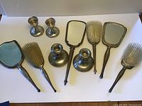All eight items arranged on white board: two mirrors, two brushes, two small beaded candlesticks, two larger candlesticks