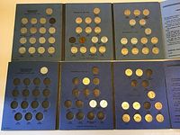 Full view of several blue folders each holding Canadian nickels arranged by years and monarchy reigns, some missing coins.