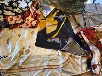 Overview of multiple silk scarves with various patterns and colors, including black and white leaves and a red and cream Van Cleef & Arpels scarf