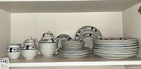 Shelf with full dinnerware set showing plates stacked and the sugar bowl, cream pitcher, and teapot with lids.