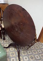 Round antique wooden table tilted vertically showing condition of the table surface and structural style with pedestal base and three feet.