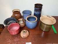 Full collection of nine pottery vases and bowls arranged on a wooden table showing their varied shapes, sizes, and glazes