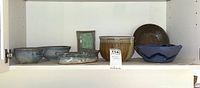Shelf with six ceramic pottery pieces: bowls, a vase, and dishes in various glazes, all artisan style.