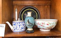 Shelf display showing the blue and white teapot, unicorn-themed vase, Asian bowl, electric candle, and enamelware platter.