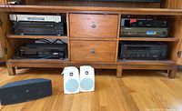 Photo of the whole electronics setup in a wood shelf including multiple black audio components and several speakers on floor.
