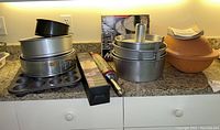 Full view of all bakeware items on kitchen counter including round tins, jumbo cupcake tin, muffin pan, rolling pin, and silicone rolling mat
