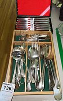Wide view of various mismatched spoons, forks, souvenir spoons, teaspoons, and tea diffuser in a wooden drawer organizer.
