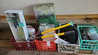 Full lot including crates with gardening and irrigation tools, tarps, boxes of irrigation parts and watering tools, placed on a wooden ledge in garage.