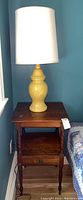 Nightstand with lamp on top, showing wood grain and surface wear.