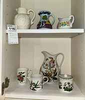 Full view of cabinet shelf with assorted pitchers and botanic themed creamer, sugar bowl, and cups