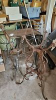 Photo showing metal patio cart and three wrought iron plant stands in garage, one stand heavily rusted
