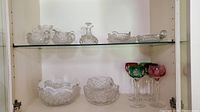 Display of multiple glass and crystal bowls, cream and sugar bowls, double handled urns, oil dish, and part of stemware on glass shelving