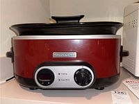 Front view of red KitchenAid slow cooker model KSC700GCO showing control dial, indicator lights, and glass lid with black handle