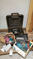 Lot contents including Makita finishing sander in box, Craftsman router in brown case, Craftsman scroller sabre saw on worn box with a red tube and manual.