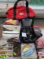 Overview of red MEC duffel bag, small white and camo tackle bags, green tackle box, gloves, reels and lure organizers on a table.