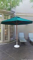 Full view of dark green patio umbrella with wooden pole and metal base on patio in daylight.