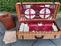 Full open picnic basket set showing wicker case, flatware, plates, containers, cups and wine carrier.
