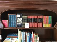 Wide view of the bookshelf with early edition books arranged side by side, showing titles and varied bindings