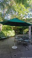 Full view of dark green canopy, wooden frame and white metal base on patio.