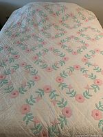 Full view of quilt spread on bed showing floral pattern and stitching