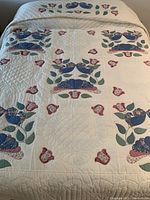 Full view of queen-sized quilt showing the overall floral and fan appliqué design in blue, pink, and green on white fabric with quilted texture.