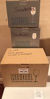 Three Riedel boxes stacked: two grey Sauternes boxes, one tan box labeled “12 white extra glasses (in case of breakage)”