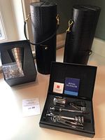 Overview of all items: wine funnel in box, wine accessory set in black box, two black wine bottle carriers.