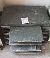Stack of roughly 12x20 inch slate tiles with a paper label indicating lot number, showing the edges and texture of the natural slate.