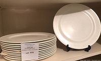 Stack of 12 white dinner plates with one displayed on stand.